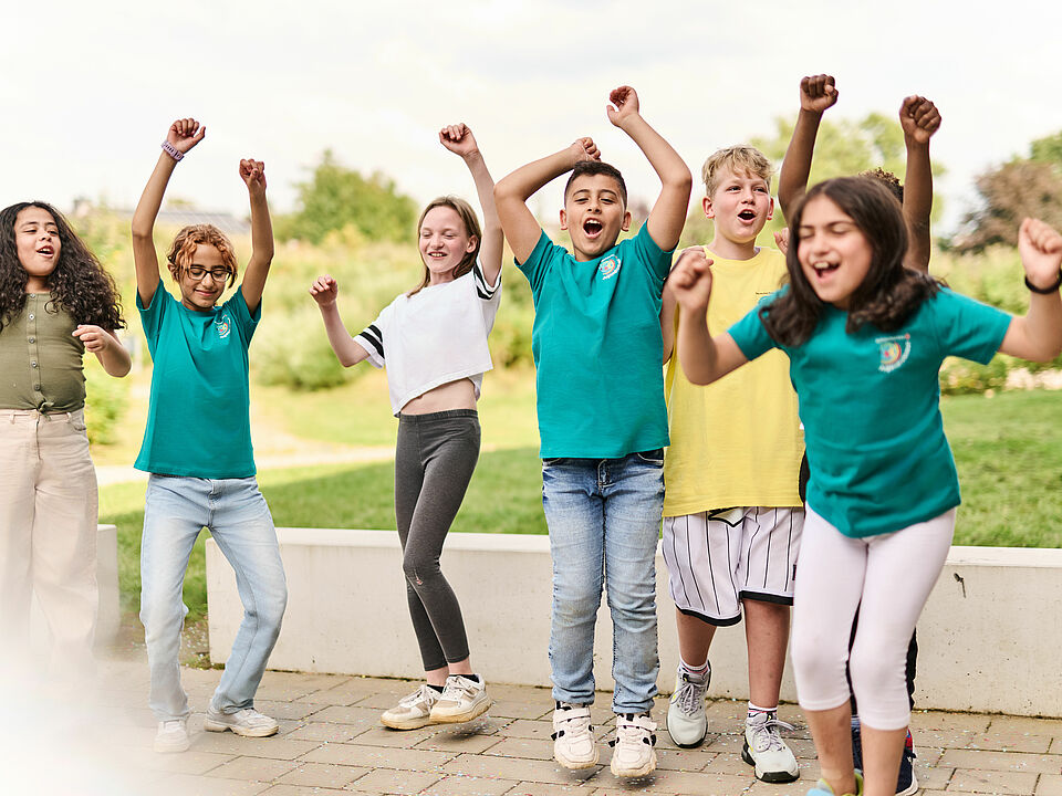 Sechs jubelnde Kinder von etwa 9 Jahren. Im Hintergrund Wiese